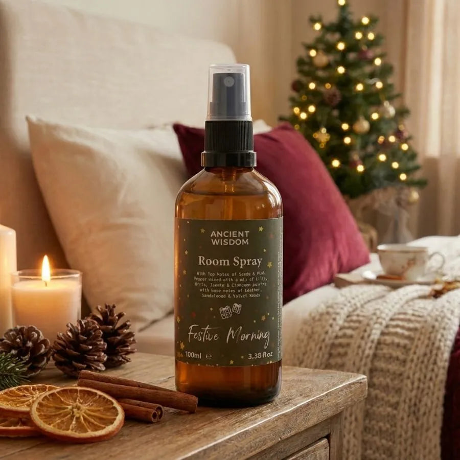 Un spray d'ambiance brume d'oreiller ancient wisdom posé sur une table de nuit avec de la cannelle et des oranges