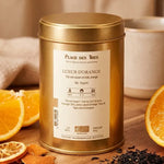 Thé noir Lueur d'Orange Bio dans sa boîte dorée avec tranches d'orange fraîches