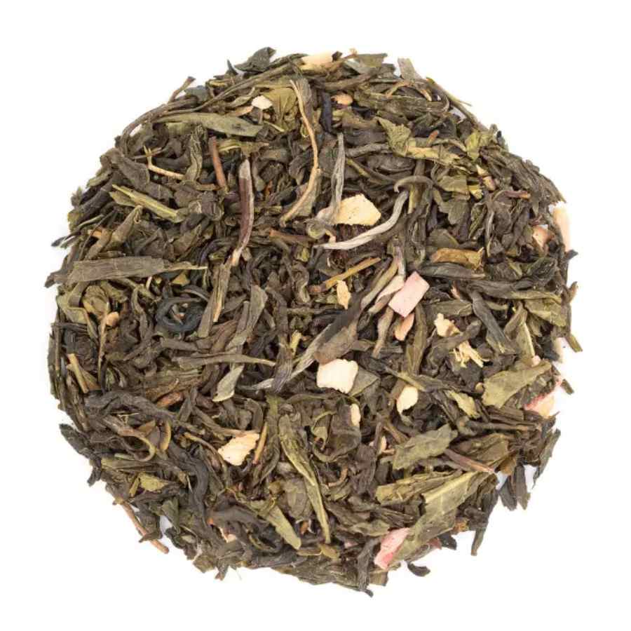 Sachet de thé vert bio « Caprice Gourmand » de la marque Les Jardins de Gaïa, aromatisé à la rhubarbe et à la fraise, présenté à côté d'un tas de feuilles de thé en vrac parsemé de morceaux de fruits.