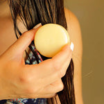Une femme en train d'appliquer sur ses cheveux le Soin Capillaire Solide à l'huile de Prune Comme avant